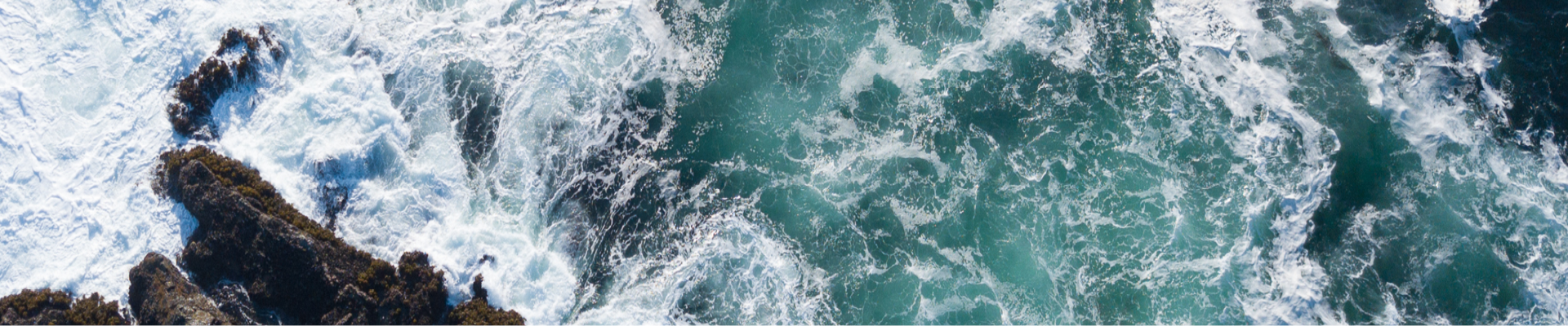 Plan d'eau bleu verdâtre avec des vagues frappant un rocher brun foncé 